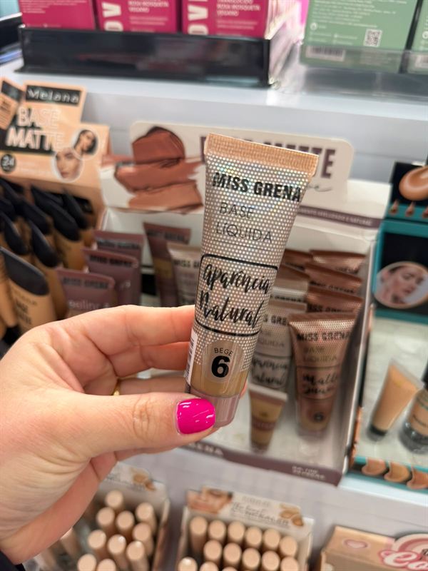 Base líquida Aparência Natural na mão, em frente ao expositor de bases